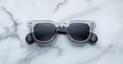 A pair of Jacques Marie Mage Vendome sunglasses by Jacques Marie Mage, featuring gray translucent frames and dark lenses, rests on a white marble surface.