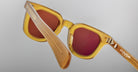 Close-up of amber-colored Jacques Marie Mage Vendome sunglasses with red-tinted lenses, photographed from behind at an angle on a plain gray background. These Jacques Marie Mage frames are expertly handcrafted in Japan.