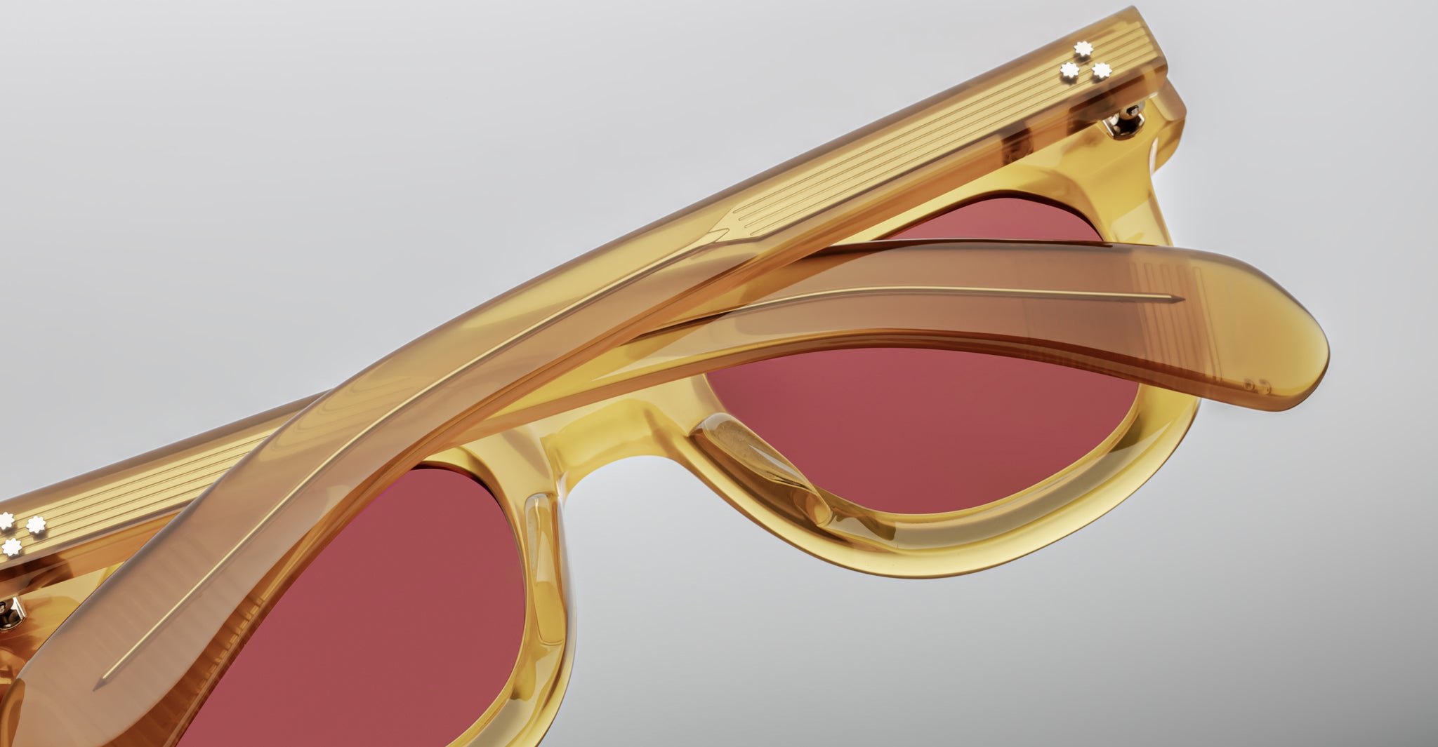 Close-up of folded translucent yellow Jacques Marie Mage Vendome sunglasses with red-tinted lenses, highlighting the brand's signature optical frames, handcrafted in Japan against a plain gray background.