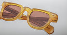 Close-up of Jacques Marie Mage Vendome sunglasses featuring yellow translucent square frames and pink-tinted lenses, handcrafted in Japan by Jacques Marie Mage, set against a plain light gray background.