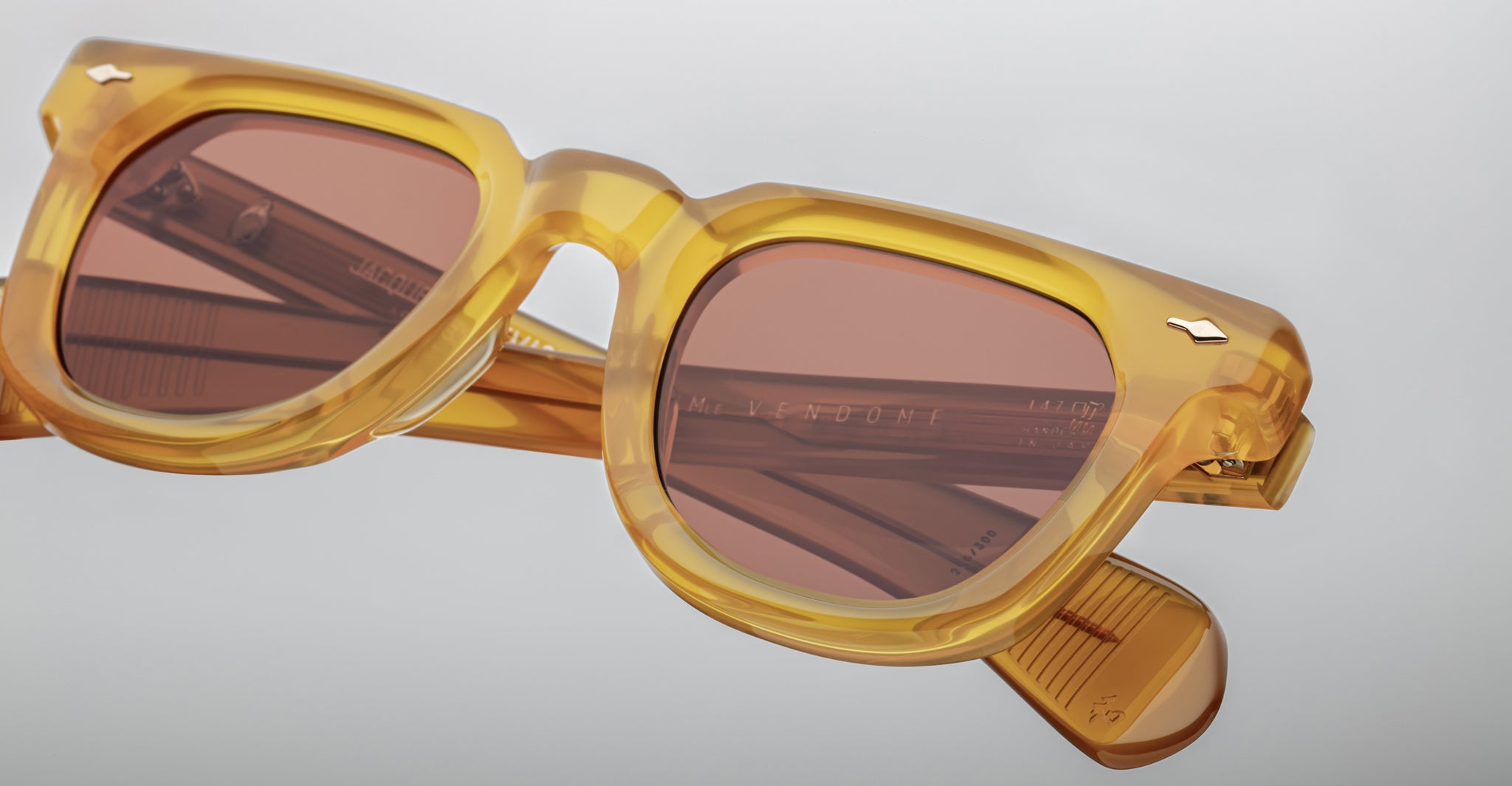 Close-up of Jacques Marie Mage Vendome sunglasses featuring yellow translucent square frames and pink-tinted lenses, handcrafted in Japan by Jacques Marie Mage, set against a plain light gray background.