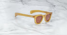 Jacques Marie Mage Vendome sunglasses with thick amber frames and brown-tinted lenses, handcrafted in Japan, are displayed on a white marble surface.