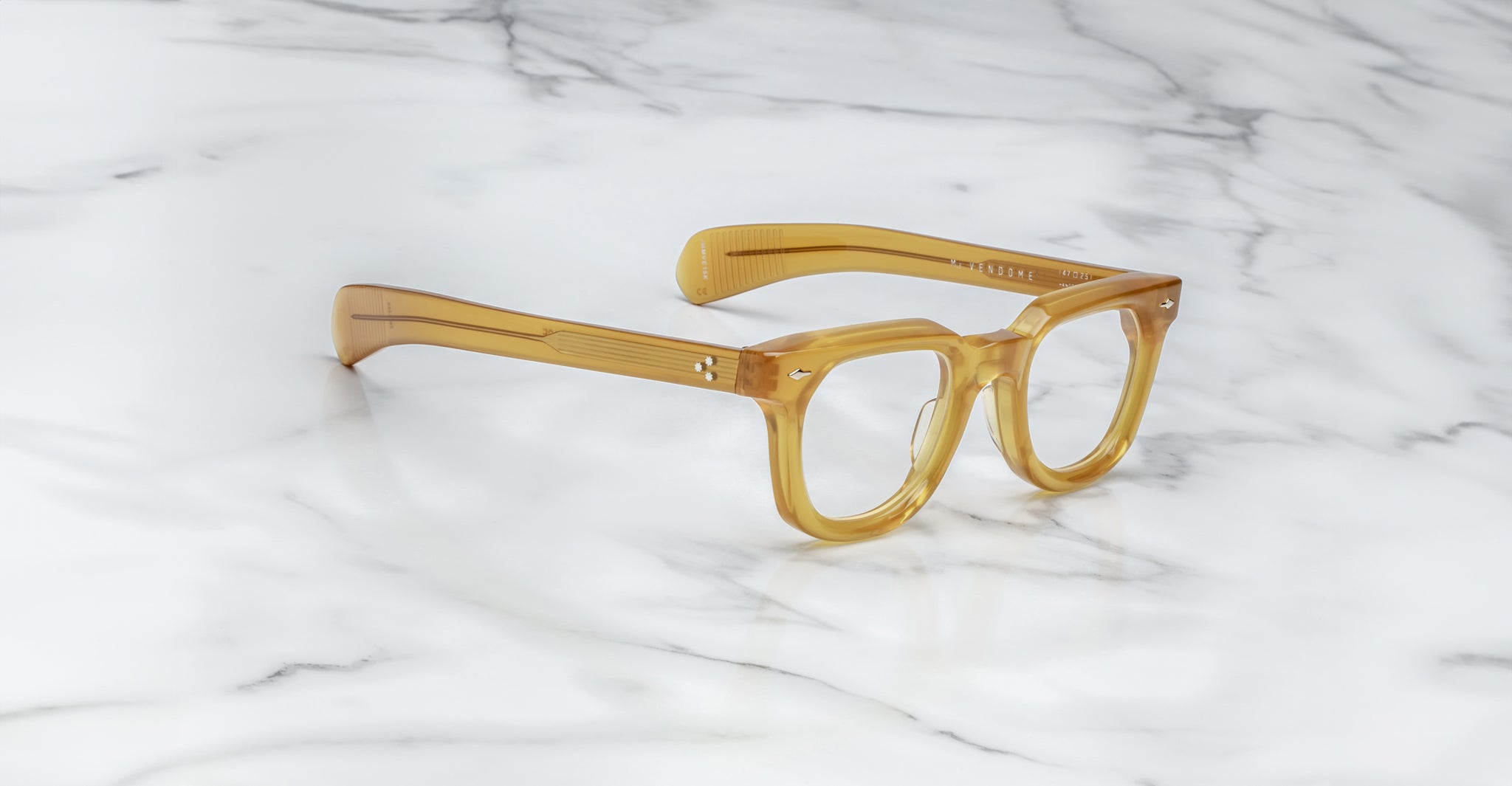 The Jacques Marie Mage Vendome by Jacques Marie Mage are thick, translucent amber rectangular optical frames handcrafted in Japan, displayed on a white marble surface.