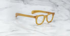 The Jacques Marie Mage Vendome by Jacques Marie Mage are thick, translucent amber rectangular optical frames handcrafted in Japan, displayed on a white marble surface.