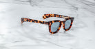Jacques Marie Mage Vendome sunglasses with a tortoiseshell pattern and blue-tinted lenses rest on white marble, highlighting the handcrafted Japanese optical frames by Jacques Marie Mage.