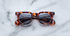 Jacques Marie Mage Vendome tortoiseshell sunglasses with dark lenses by Jacques Marie Mage, handcrafted in Japan, displayed on a white marble surface.