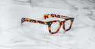 A pair of Jacques Marie Mage Vendome optical frames from Jacques Marie Mage, featuring a thick tortoiseshell design handcrafted in Japan, rests on a white marble surface.