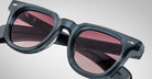 Close-up of Jacques Marie Mage Vendome sunglasses by Jacques Marie Mage, featuring thick frames and pink lenses, handcrafted in Japan, set against a gray background.