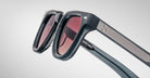 Close-up of Jacques Marie Mage Vendome sunglasses, handcrafted in Japan with thick black frames, red-tinted lenses, and striped detailing on the arms.