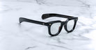 Jacques Marie Mage Vendome by Jacques Marie Mage: black thick-rimmed optical frames with clear lenses, handcrafted in Japan, displayed on a white marble surface.