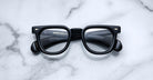 Jacques Marie Mage Vendome black rectangular optical frames by Jacques Marie Mage, featuring thick rims and handcrafted in Japan, are displayed elegantly on a white marble surface in an overhead view.