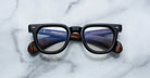 The Jacques Marie Mage Vendome by Jacques Marie Mage are black rectangular optical frames, handcrafted in Japan, featuring visible text on the inner arms and displayed on a white marble surface.