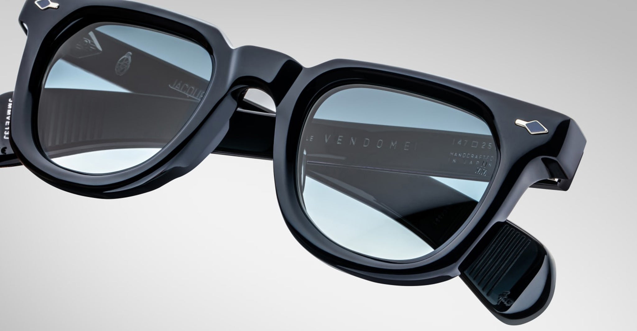 Close-up of Jacques Marie Mage Vendome optical frames by Jacques Marie Mage, handcrafted in Japan with black rectangular design, silver accents, blue-tinted lenses, and Le Vendome plus model details inside the frame.