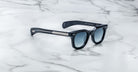 Jacques Marie Mage Vendome sunglasses by Jacques Marie Mage, handcrafted in Japan with blue lenses and silver-accented temples, shown on a white marble surface.