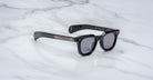 The Jacques Marie Mage Vendome sunglasses by Jacques Marie Mage feature black rectangular frames with dark lenses, handcrafted in Japan, and are displayed on a white marble surface.