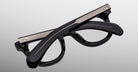 The Jacques Marie Mage Vendome black optical frames, featuring metallic accents, are shown folded on a light gray background. Handcrafted in Japan, these eyeglasses by Jacques Marie Mage offer timeless style and artisanal quality.
