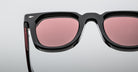 Close-up of Jacques Marie Mage Vendome sunglasses, featuring black frames and pink-tinted lenses, handcrafted in Japan, displayed on a plain light gray background.