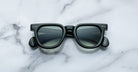 A pair of Jacques Marie Mage Vendome sunglasses in black with square frames and dark lenses, handcrafted in Japan, sits on a white marble surface.