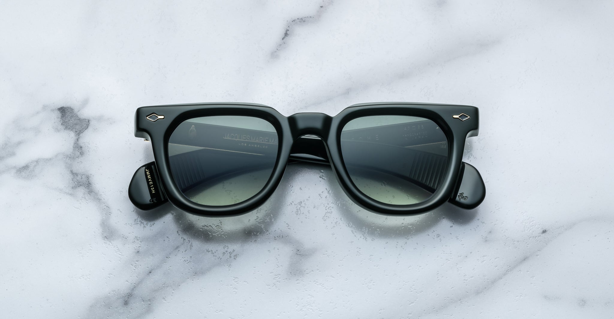 A pair of Jacques Marie Mage Vendome sunglasses in black with square frames and dark lenses, handcrafted in Japan, sits on a white marble surface.