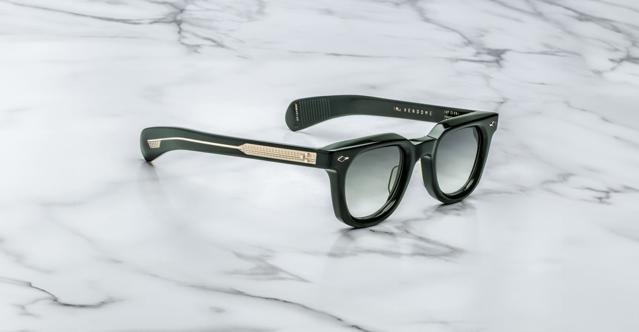 Jacques Marie Mage Vendome black sunglasses with dark lenses and gold-detailed arms, handcrafted in Japan, displayed on a white marble surface.