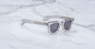 Jacques Marie Mage Vendome clear-frame sunglasses with dark lenses, handcrafted in Japan by Jacques Marie Mage, displayed on a white marble surface.