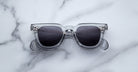 Jacques Marie Mage Vendome sunglasses featuring clear frames and dark lenses, from Jacques Marie Mage, displayed on a white marble surface.