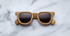 Tan square-framed Jacques Marie Mage Vendome sunglasses with dark lenses by Jacques Marie Mage, handcrafted in Japan, shown on a white marble surface.