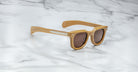 Tan plastic Jacques Marie Mage Vendome sunglasses with dark lenses and thick frames are placed on a white marble surface.