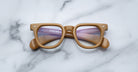Jacques Marie Mage Vendome optical frames by Jacques Marie Mage, featuring brown square frames and purple-tinted lenses, are displayed on a white marble surface.