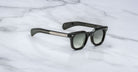 The Jacques Marie Mage Vendome sunglasses by Jacques Marie Mage, featuring thick frames and dark gradient lenses handcrafted in Japan, are elegantly displayed on a white marble surface.