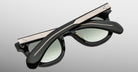 A pair of Jacques Marie Mage Vendome black sunglasses by Jacques Marie Mage, featuring metal accents and handcrafted in Japan, are folded and displayed on a light gray background.