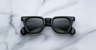 Jacques Marie Mage Vendome black rectangular sunglasses with dark lenses by Jacques Marie Mage, handcrafted in Japan, shown on a white marble surface.