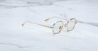 Jacques Marie Mage Verlaine gold hexagonal eyeglasses with clear lenses shown from above on a white marble surface.