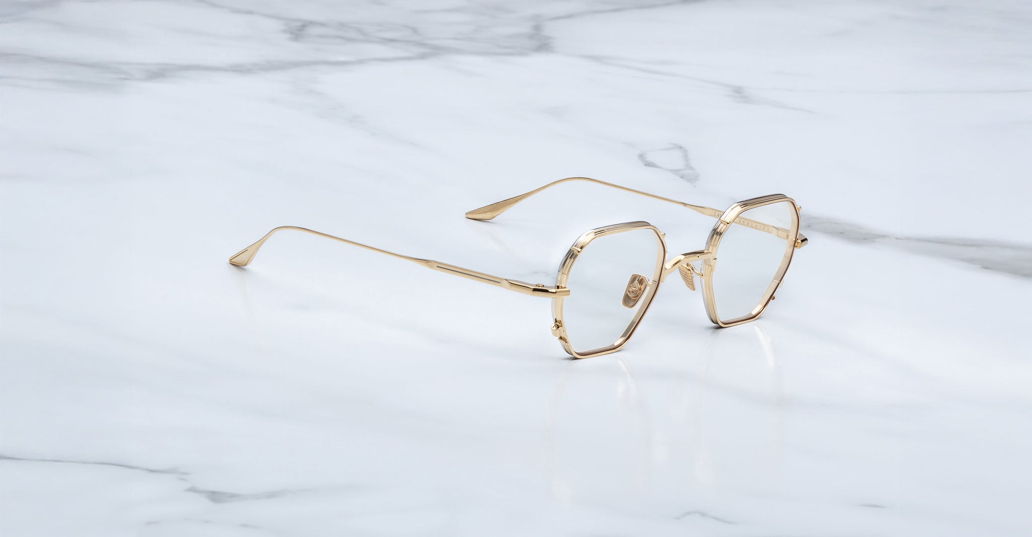 Jacques Marie Mage Verlaine gold hexagonal eyeglasses with clear lenses shown from above on a white marble surface.