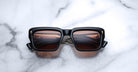 Jacques Marie Mage Walker sunglasses, black frame with brown lenses, shown from above with reflected stripes.