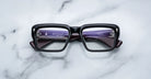 Jacques Marie Mage Walker eyeglasses with thick black rims and purple inner arms, viewed from above.