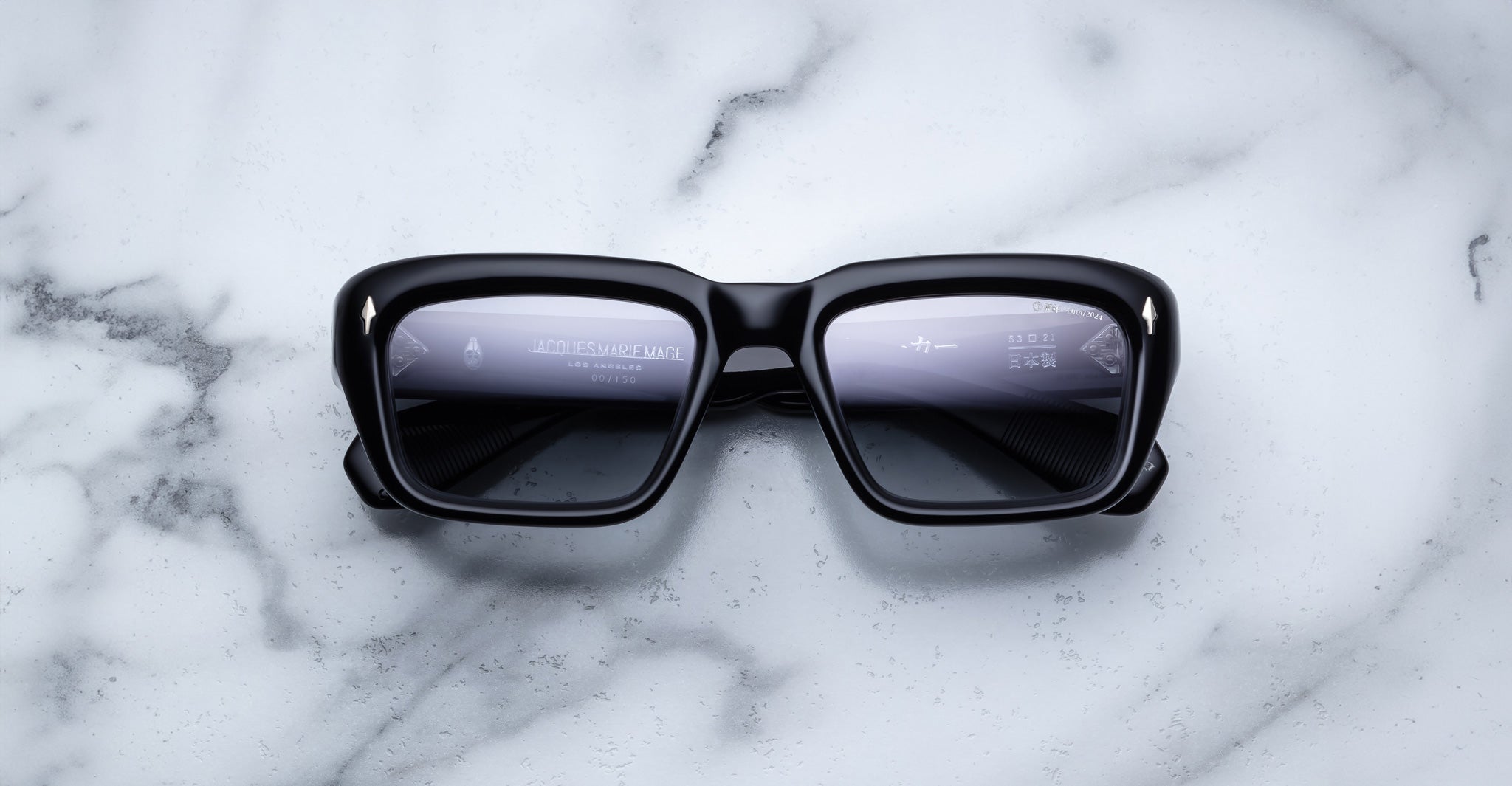 Jacques Marie Mage Walker smart sunglasses with reflective lenses, shown from above, on a flat surface.