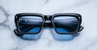 Jacques Marie Mage Walker black rectangular sunglasses with blue-tinted lenses, shown from above.