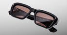 Jacques Marie Mage Walker sunglasses feature black rectangular frames with thick construction and brown-tinted lenses, shown on a light gray background. The WALKER name appears on the inside of one arm.