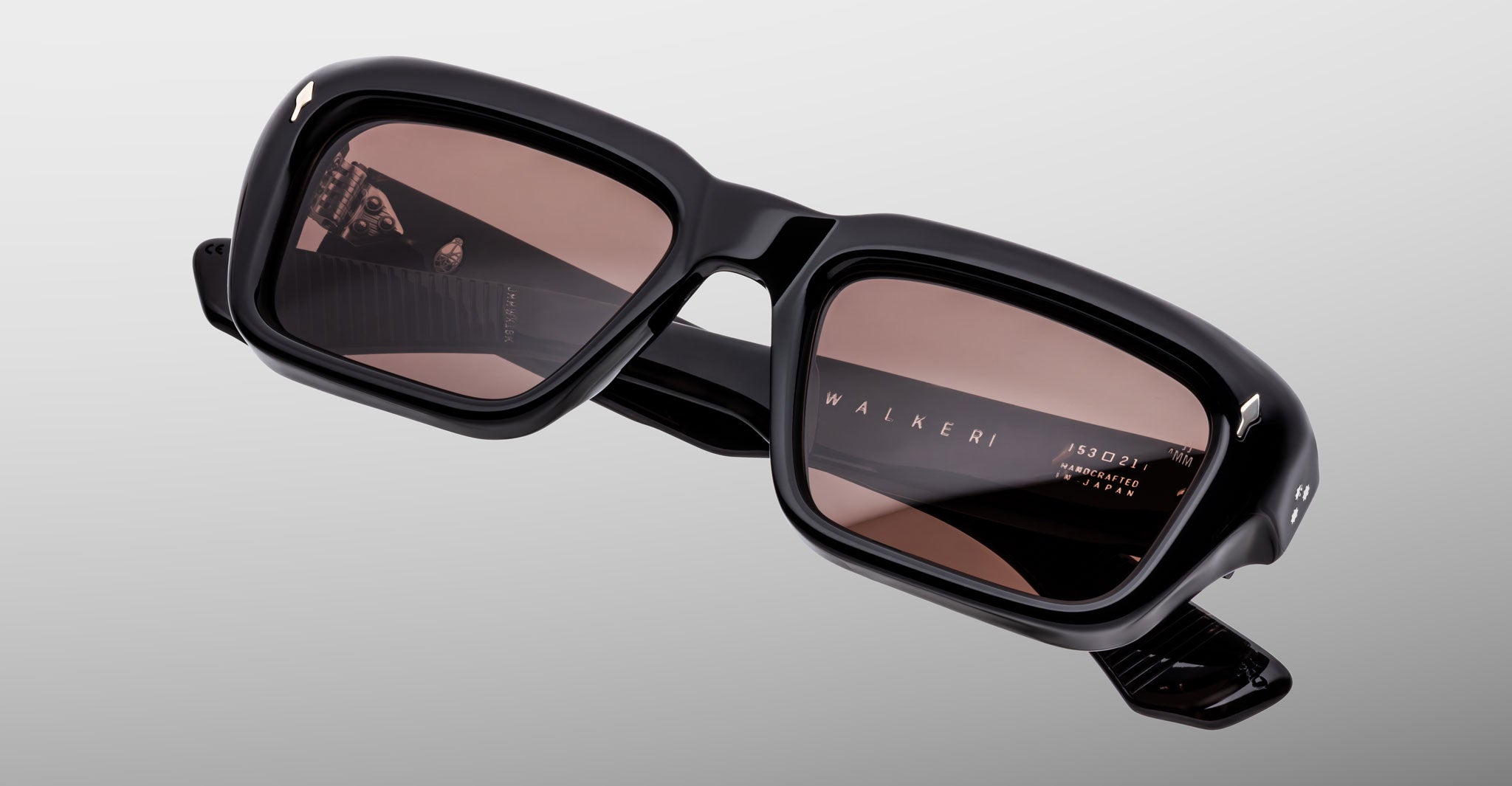 Jacques Marie Mage Walker sunglasses feature black rectangular frames with thick construction and brown-tinted lenses, shown on a light gray background. The WALKER name appears on the inside of one arm.