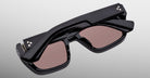 The Jacques Marie Mage Walker is a pair of black, futuristic smart glasses with rectangular tinted lenses and built-in electronics on the temples, displayed folded against a light gray background.