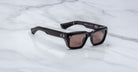 Jacques Marie Mage Walker black rectangular sunglasses with thick frames and dark tinted lenses rest on a white marble surface.