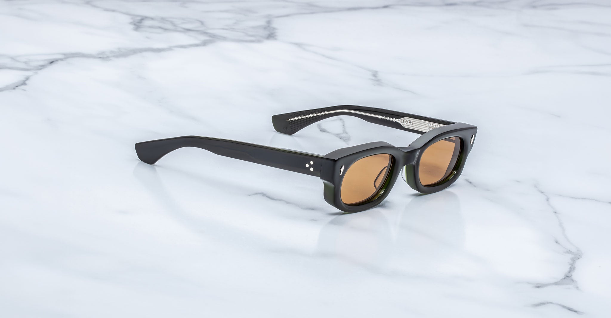Jacques Marie Mage Whiskeyclone in Borneo dark green acetate sunglasses with translucent olive green accents, warm amber-tinted lenses, signature silver-tone arrowhead rivets, and three-dot temple detailing, shown in a three-quarter angled view on a white marble surface