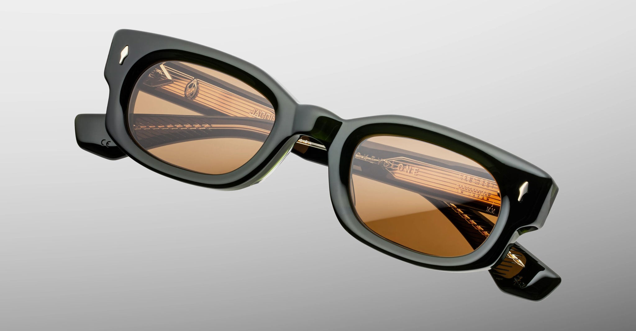 Jacques Marie Mage Whiskeyclone in Borneo, dark green acetate sunglasses with translucent olive green accents, warm amber-tinted lenses, signature silver-tone arrowhead rivets, and visible engraved metal core temples, shown in an angled front close-up highlighting the sculpted frame and intricate interior detailing