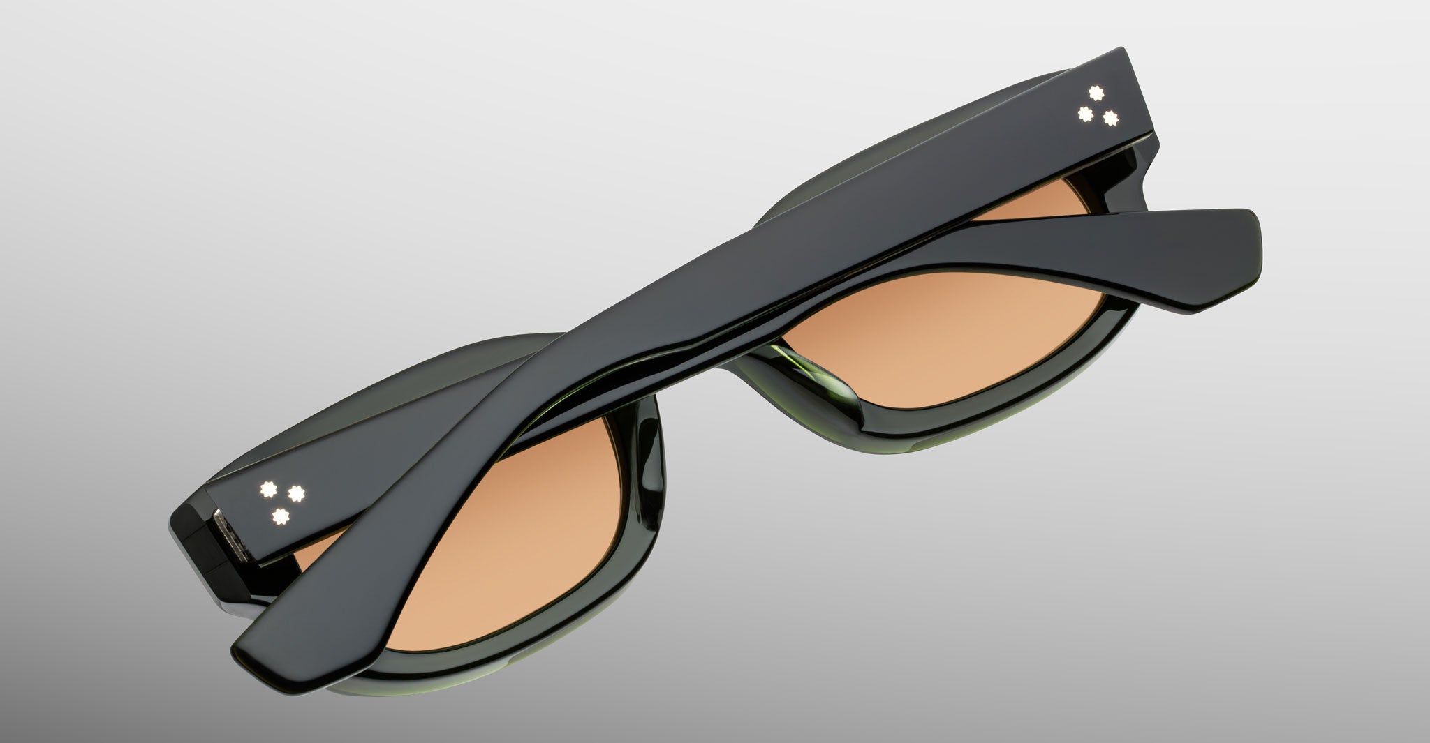 Jacques Marie Mage Whiskeyclone in Borneo, dark green acetate sunglasses with warm amber-tinted lenses and signature three-dot silver-tone rivets, shown folded in a close-up detail view highlighting the sculpted frame and wide acetate temples