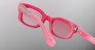 Close-up of Jacques Marie Mage Whiskeyclone sunglasses with thick pink frames and pink-tinted lenses. The plain light gray background highlights the prominent left temple arm with a silver metal detail.