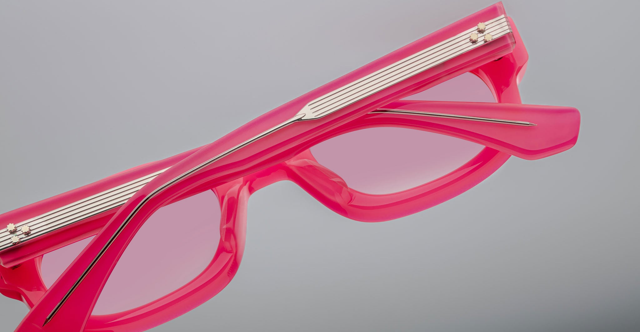 A close-up of Jacques Marie Mage Whiskeyclone sunglasses with bright pink, pink-tinted lenses and metallic arm detailing, set against a plain light gray background.