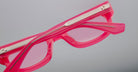 A close-up of Jacques Marie Mage Whiskeyclone sunglasses with bright pink, pink-tinted lenses and metallic arm detailing, set against a plain light gray background.