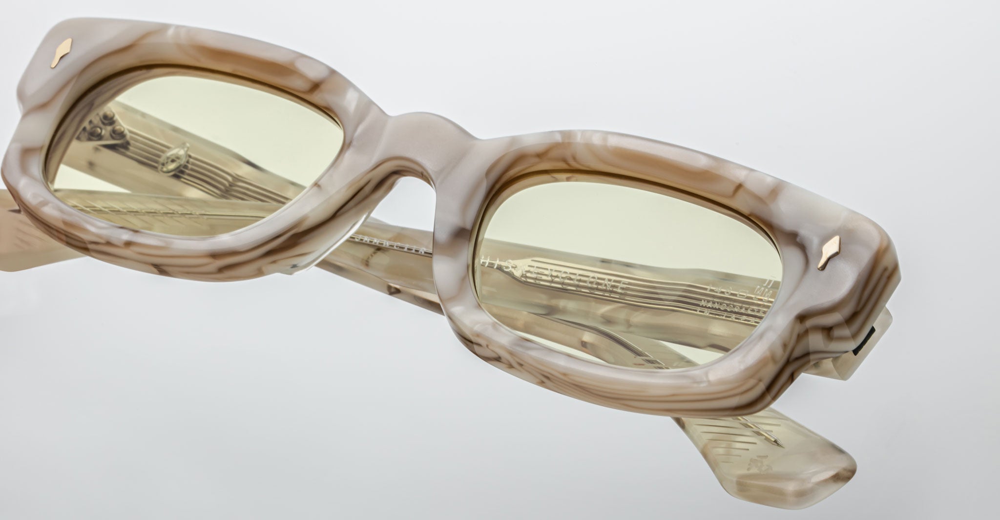 Close-up of Jacques Marie Mage Whiskeyclone rectangular eyeglasses with thick marbled beige and brown frames, light yellow-tinted lenses, isolated on a plain white background.