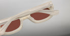 A close-up of Jacques Marie Mage Whiskeyclone sunglasses, featuring a cream-colored translucent frame, brown lenses, metallic hinges, and a minimalist modern design, shown folded against a plain background.